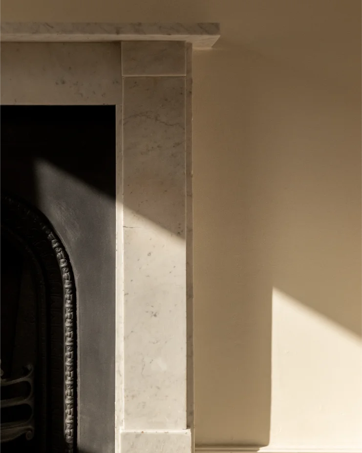 Marble fireplace with sunlight casting shadows.