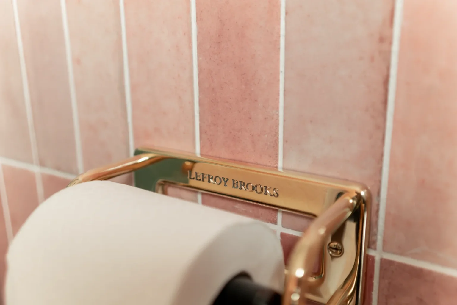 Gold toilet paper holder on pink tiled wall.