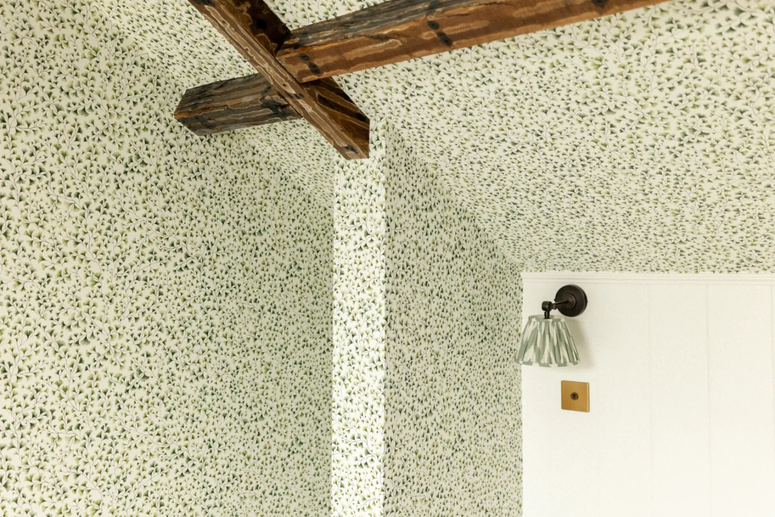 Floral wallpaper with wooden beams and wall sconce.