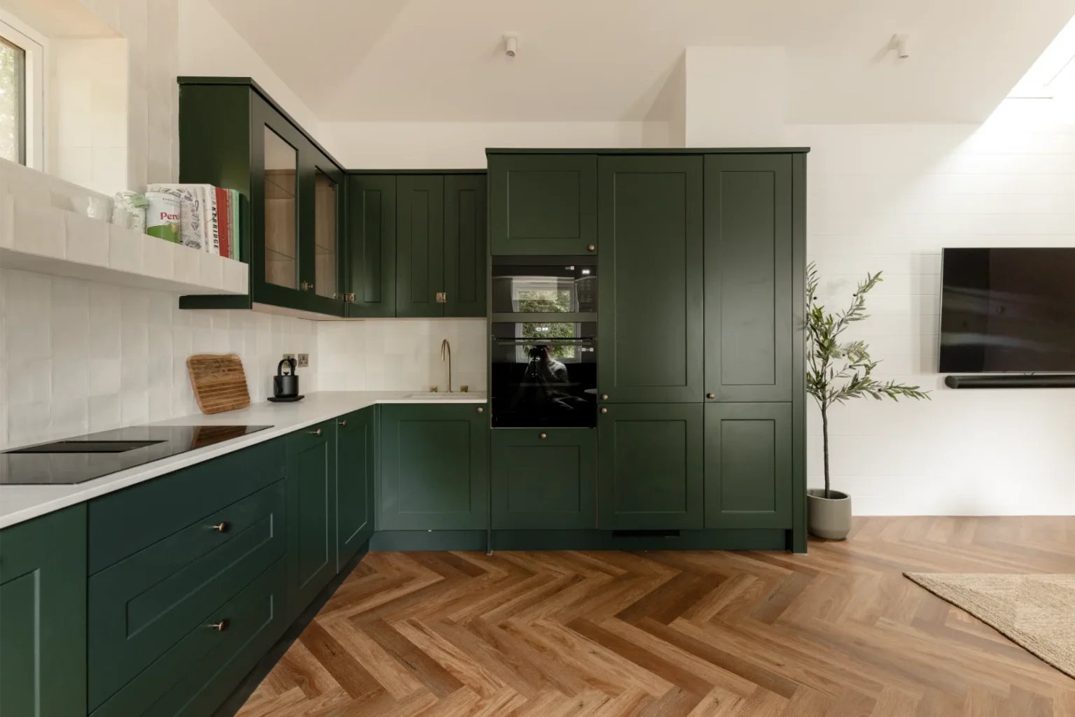 Modern kitchen with green cabinets and herringbone floor.
