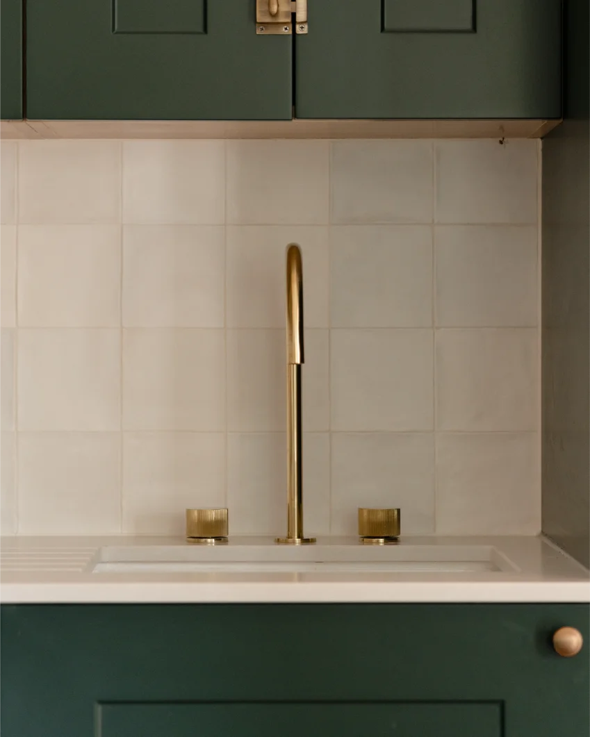 Modern kitchen sink with gold faucet and green cabinets.