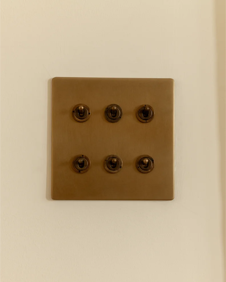 Vintage brass light switch panel on wall.