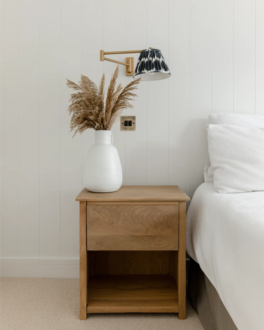 Wooden nightstand with lamp and vase in bedroom.