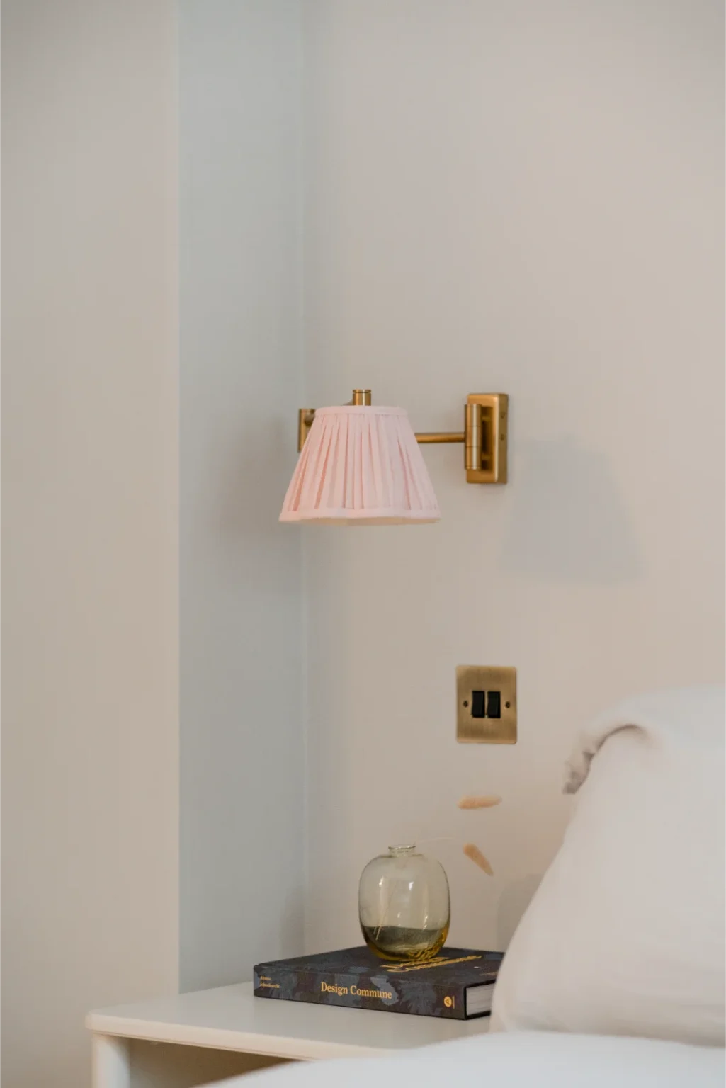 Bedroom wall sconce above nightstand with book and vase.