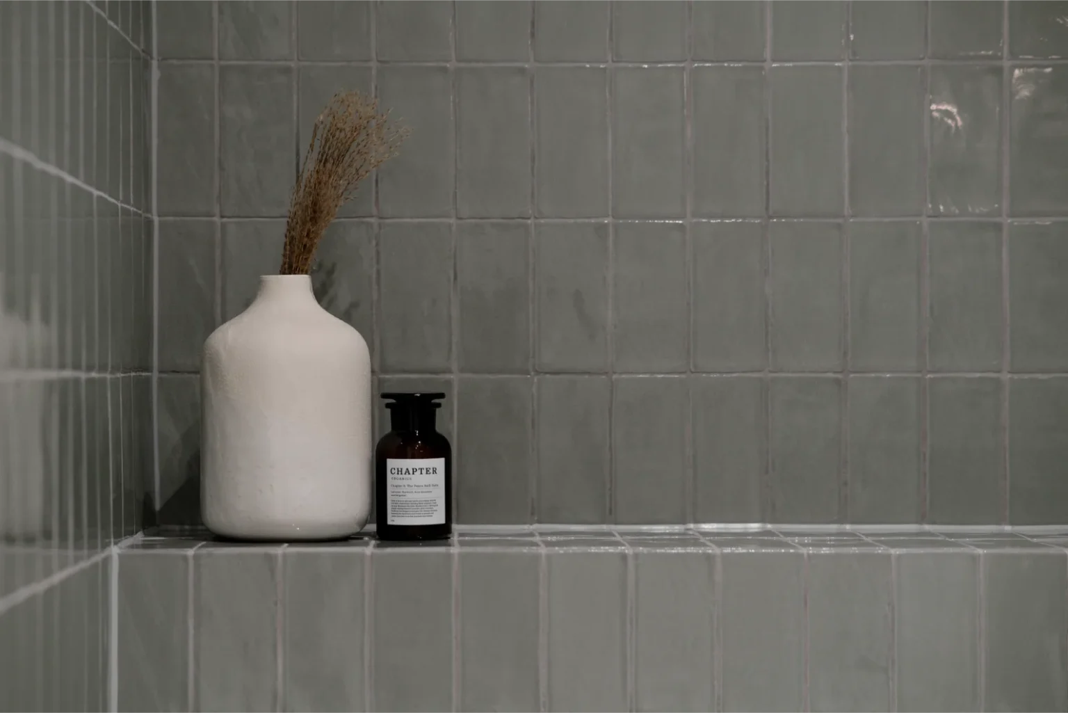 Ceramic vase and bottle on tiled shelf