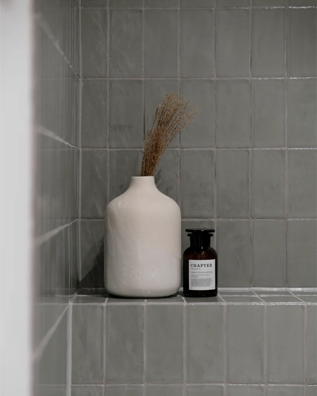 Ceramic vase and bottle on tiled shelf.