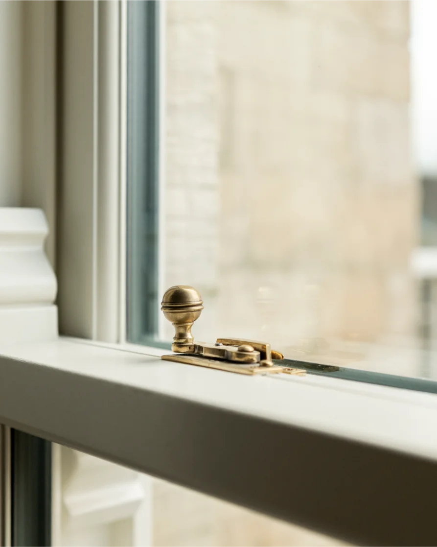Close-up of brass window latch on wooden frame.