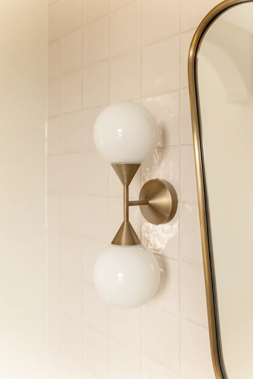 Brass wall sconce with round bulbs near mirror.