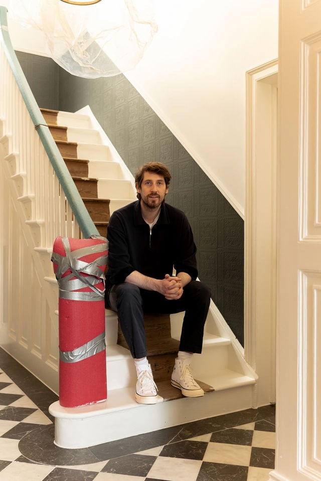 Man sitting on staircase with red railing.
